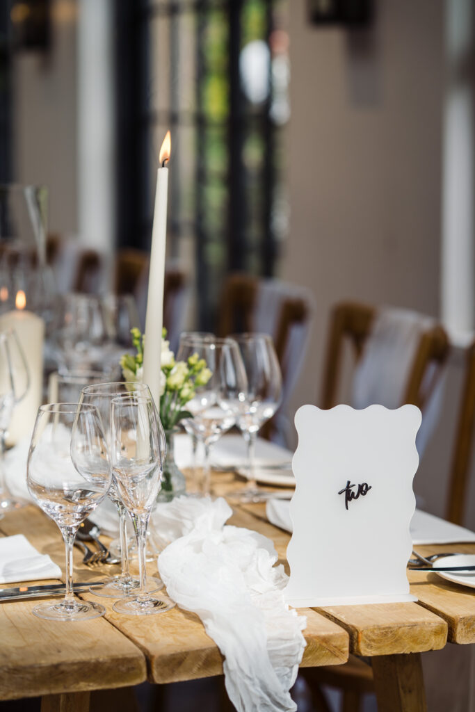 Close-up of a Middleton Lodge reception table with wine glasses, taper candle, linen details and table number sign.