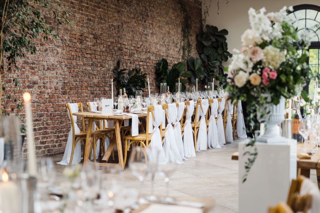 Long banquet table in the Middleton Lodge orangery with a brick wall backdrop, candlelit place settings and floral arrangements.